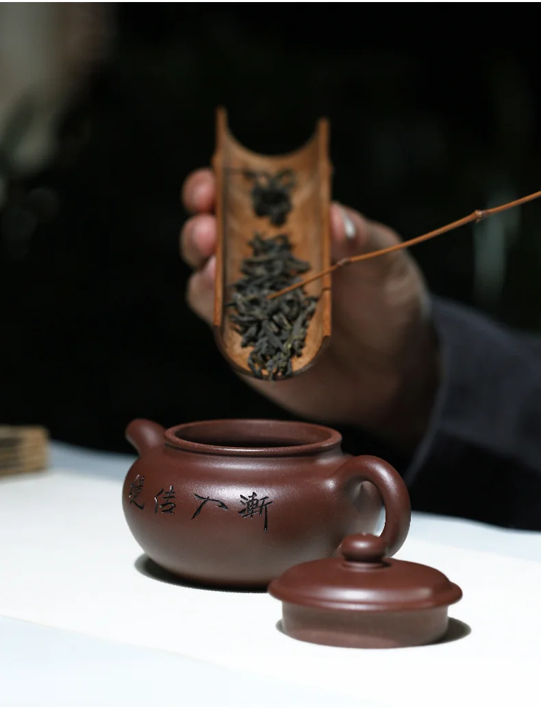 Tea leaves being added to an open clay teapot with a tea scoop